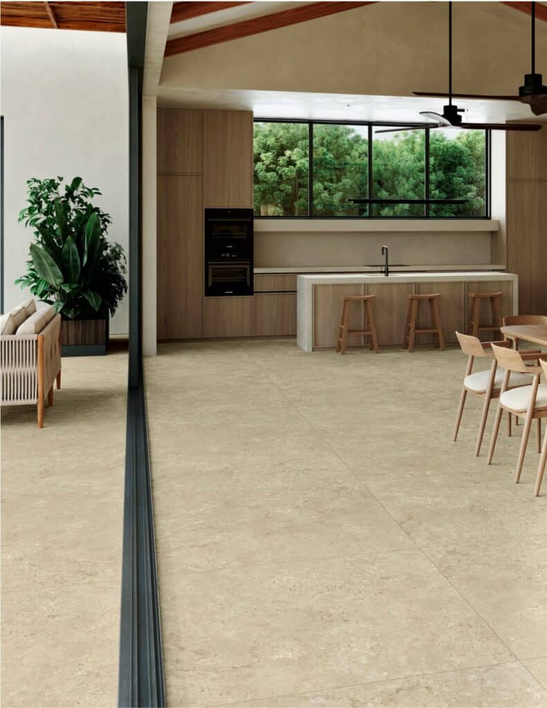 Sol en carrelage beige effet pierre dans une cuisine moderne boisée avec vue sur jardin.