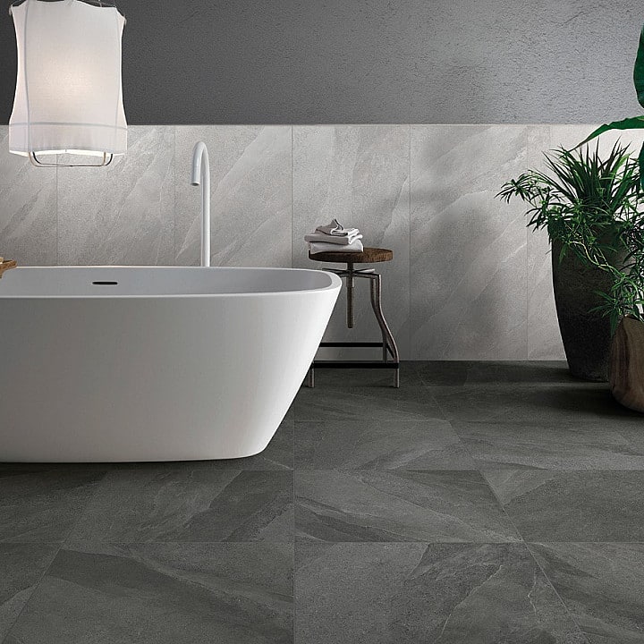 Baignoire îlot blanche moderne dans une salle de bain aux tons gris, avec carrelage effet ardoise sombre et mur clair.